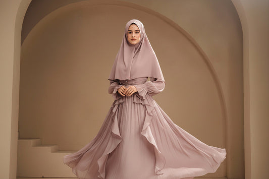 Woman in a flowing pink dress with intricate details, standing against a neutral background.