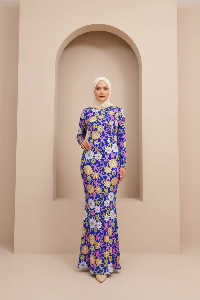 Woman wearing a floor-length, long-sleeve blue floral modest gown standing in front of a neutral arched wall.
